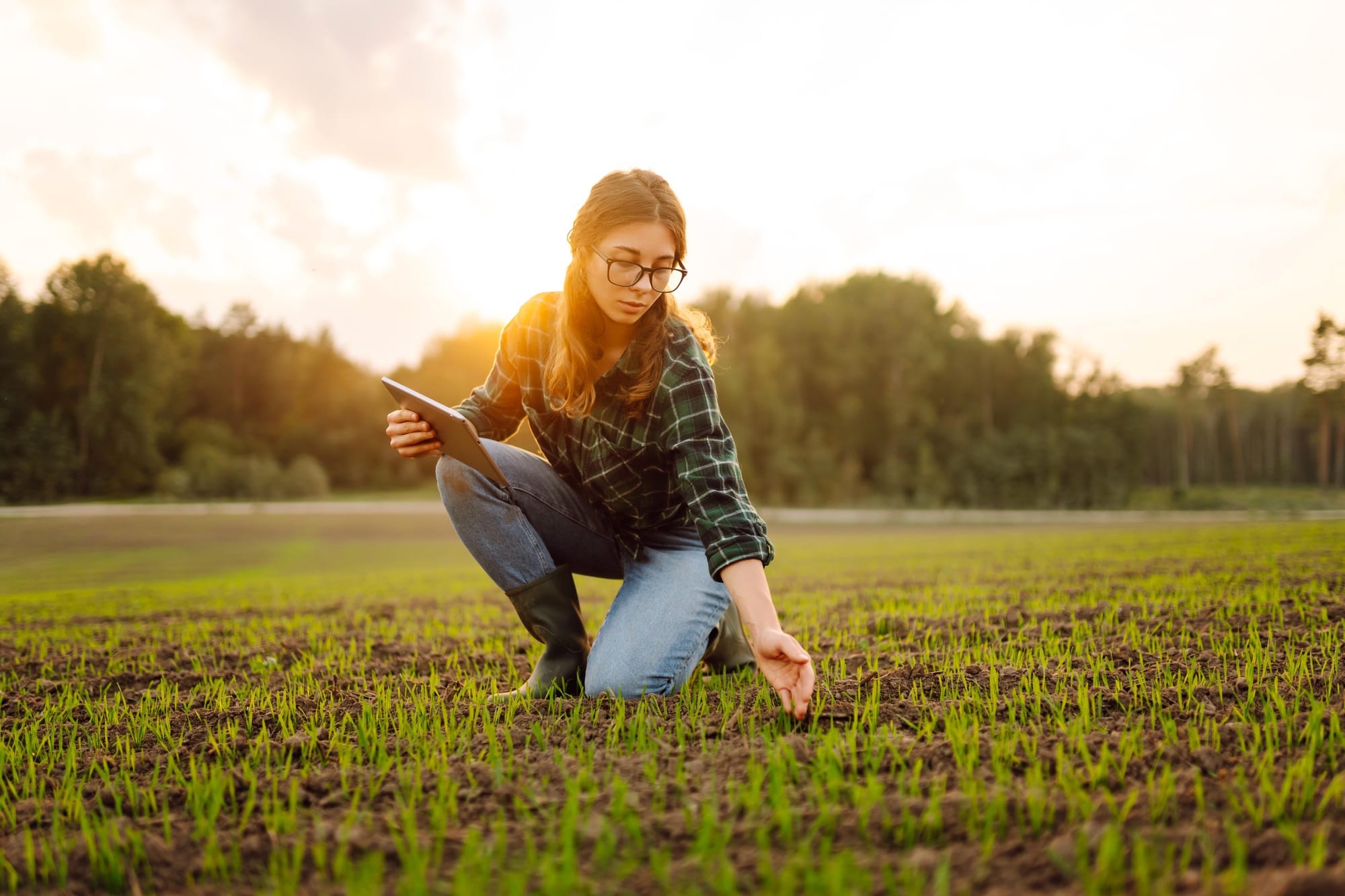 Farmer woman in boots checks the quality of the soil before sowing in her hands with digital tablet.